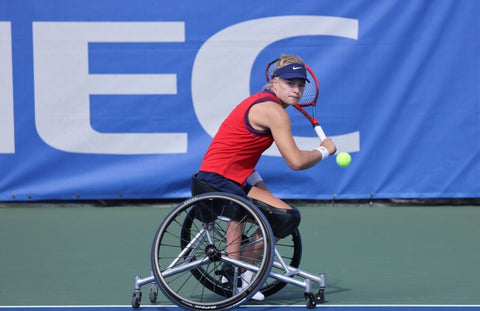 Paralympian athlete in a wheelchair about to strike a tennis ball with her racquet.