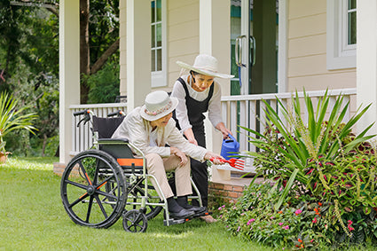 Two women gardening, one in a wheelchair watering outdoor plants