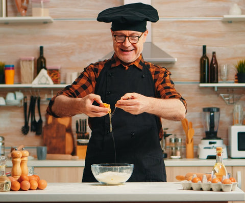 A photograph of a chef cracking eggs into a bowl of flour. He looks happy to be baking.