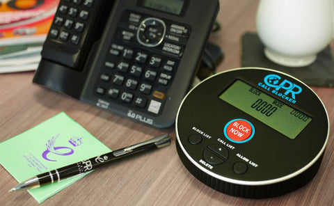 The Call Blocker – V10000 is on a wooden desk, next to a telephone