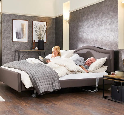 This is an image of the Opera Comfort Dual Profiling Bed with an elderly couple in it. One of them is sleeping whilst the other had used the adjustable backrest to sit up and read a book.