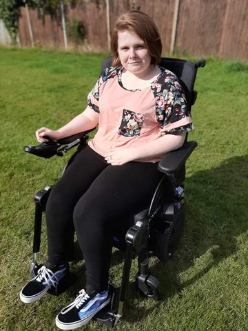 Ami sitting in her new wheelchair – the wheelchair is in the garden and Ami is looking out towards the viewer