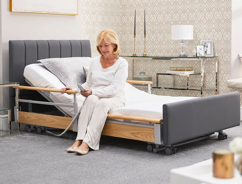 An image of the Opera Solo Comfort Plus. This bed has side rails for safety. There is a woman sat on the edge using the mattress profiling platform remote control.