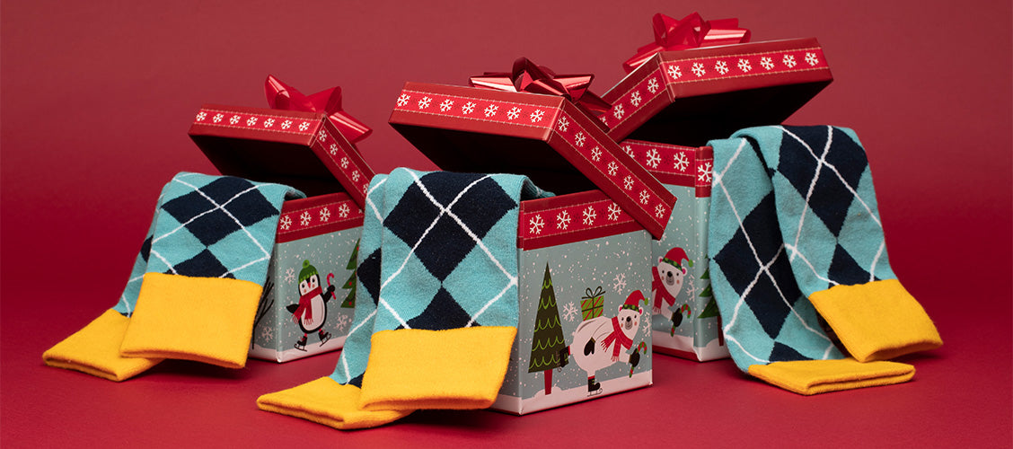 Men's, women's, and kids' matching socks in an argyle pattern hanging out of different sized Christmas boxes - Family Gift Ideas