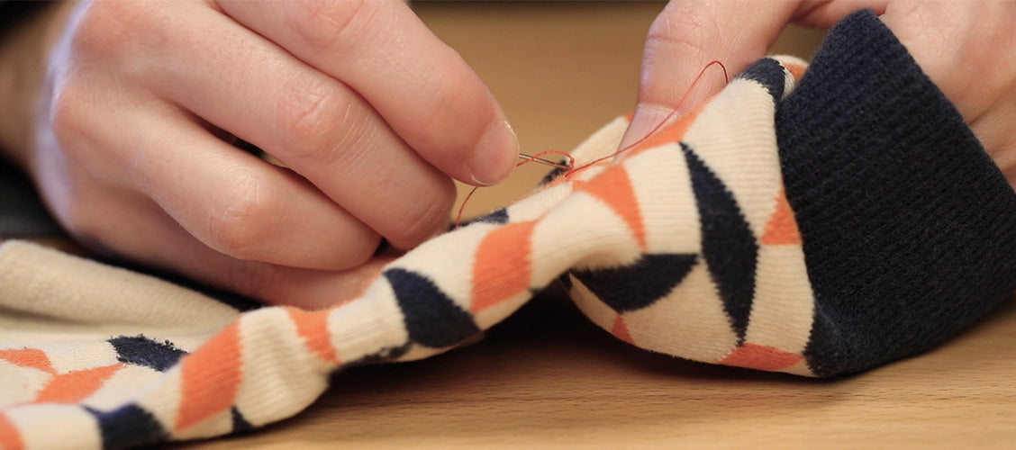 Threaded sewing needle being inserted into socks at the base of a snag