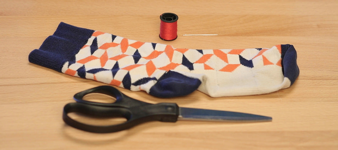 Sock with a snag laying on a craft table with a spool thread, a sewing needle, and scissors
