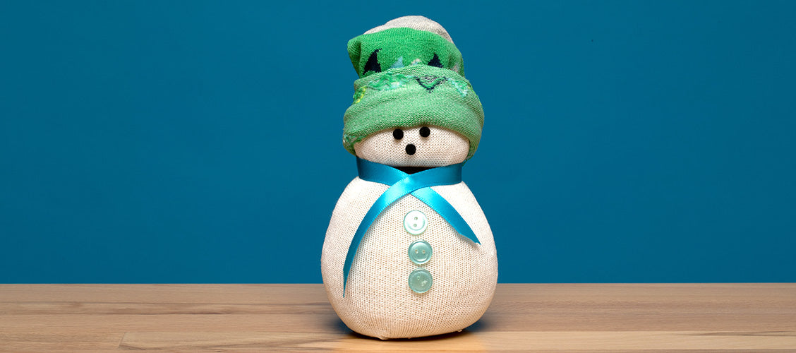 Snowman made out of white and green socks sitting on a craft table - How to Make a No-Sew Sock Snowman