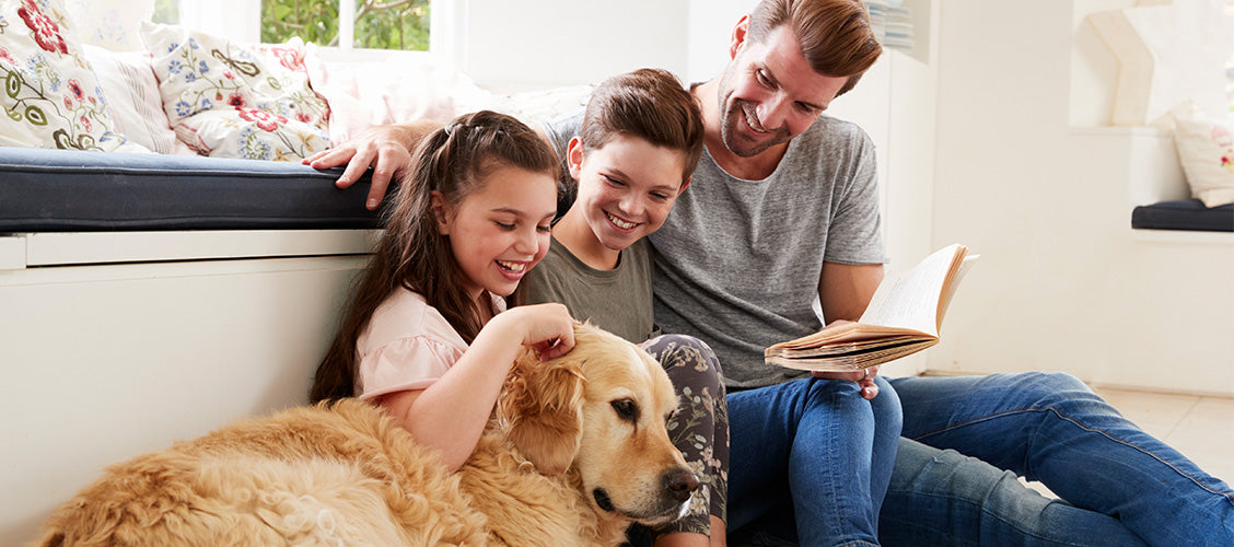 Family sitting on floor reading book with golden retriever dog - Best Pets for Kids