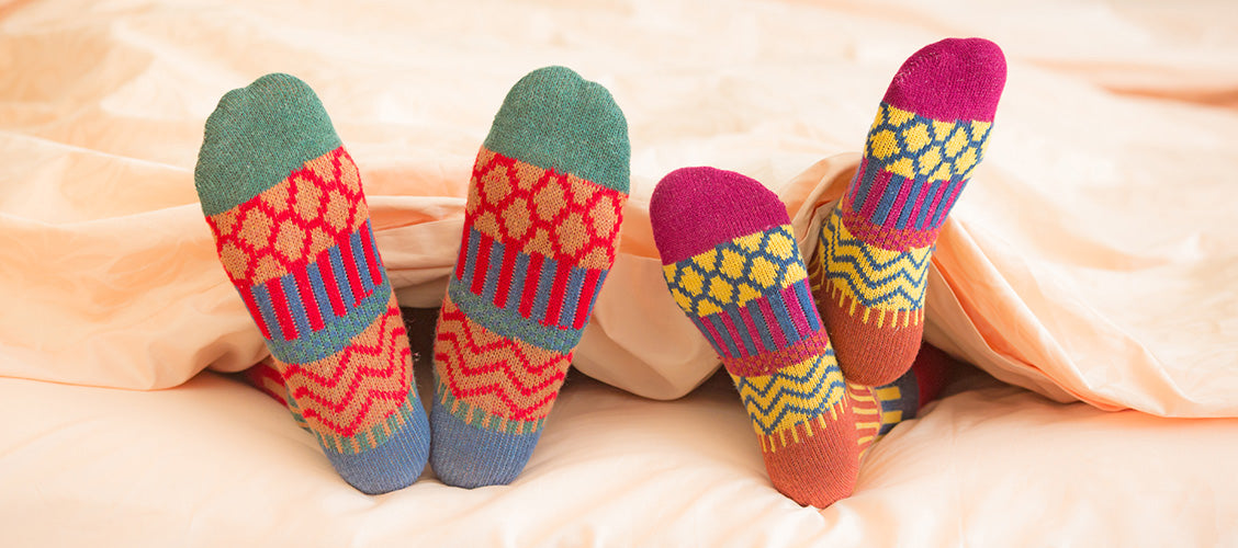 Two people laying in bed with their colorful socks sticking out of the sheets - 7 Reasons to Wear Fun Socks