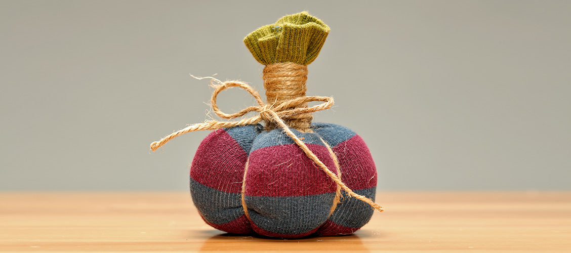 Small pumpkin made out of a sock and twine sitting on a craft table - How to Make a Sock Pumpkin