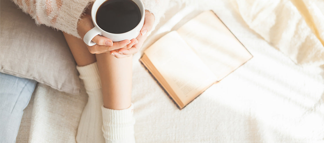 Woman in cream socks holding a warm cup of coffee - 10 Ways to Keep Your Feet Warm