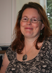 Close-up of author smiling in a kitchen, wearing glasses, and a necklace with a dolphin pendant on it.