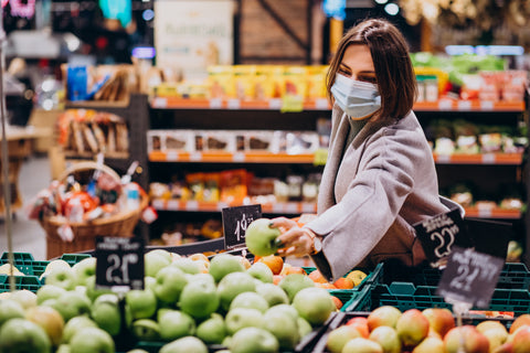 women grabbing a green apple wearing a mask in the grocery store