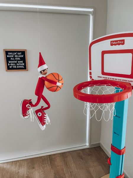 The Elf of the Shelf slam dunks a toy basketball into a basketball hoop.
