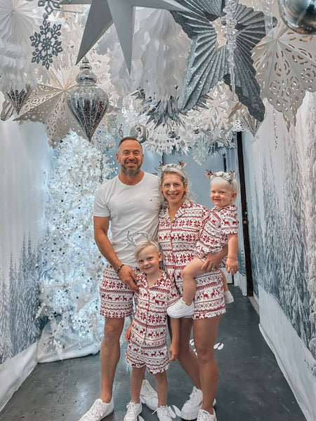 The Shaw family, dressed in matching Christmas outfits, pose together in front of a white Christmas scene.