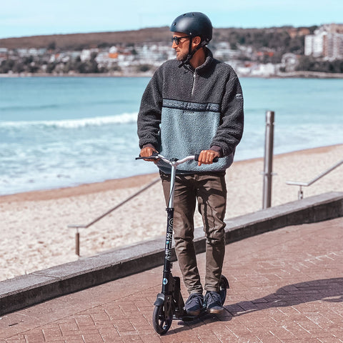 adult riding 2 wheel kick scooter along the beach