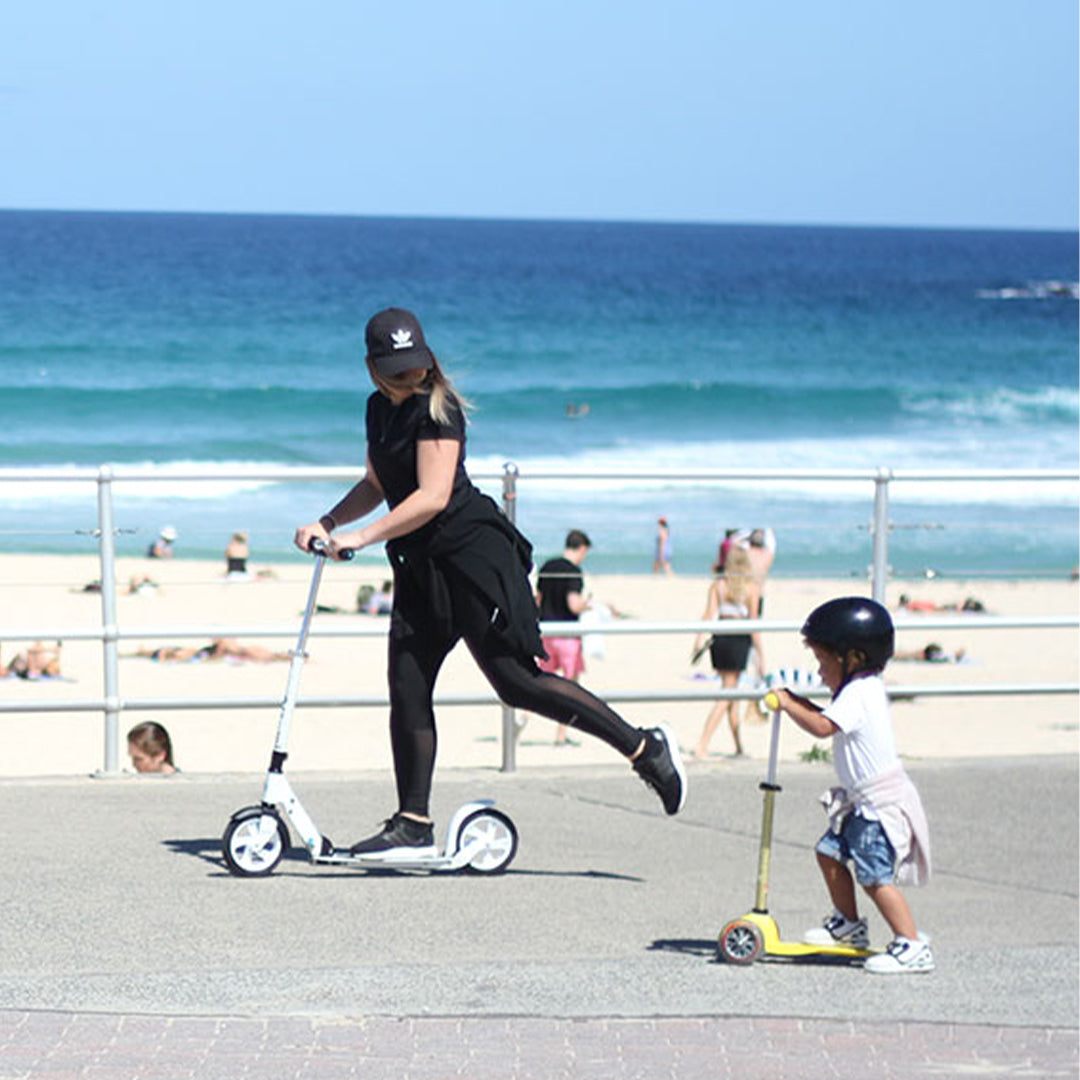 adult and toddler riding their micro scooters along the beach