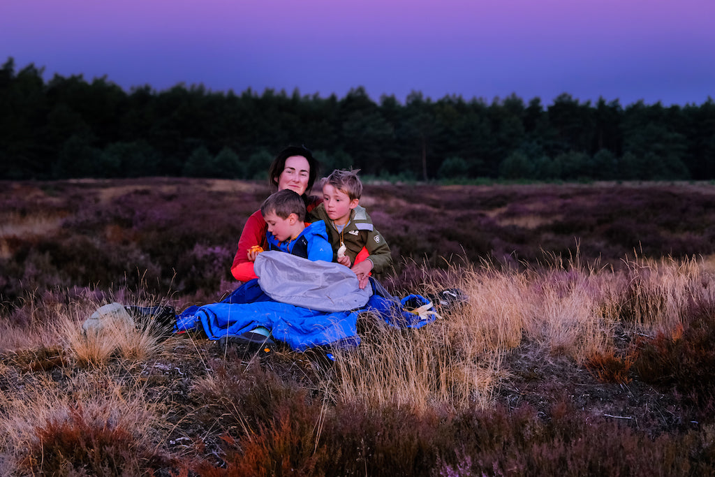 Mum and sons watching the sunrise in their sleeping bags