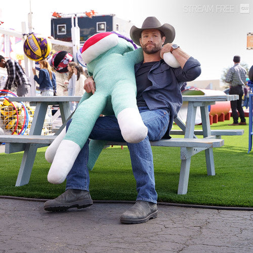 Jared Padalecki sits on a bench holding a stuffed puppet