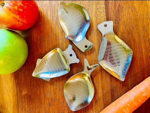 Steel Sea Animal Graters with Fruits and Carrot on Wooden Surface