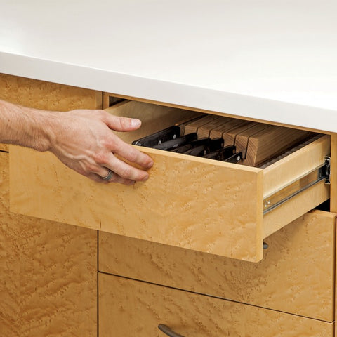 A close-up of a push to open drawer guide mechanism installed on a cabinet drawer. The mechanism has a silver finish and is shown in the open position, with the drawer extended outwards from the cabinet.