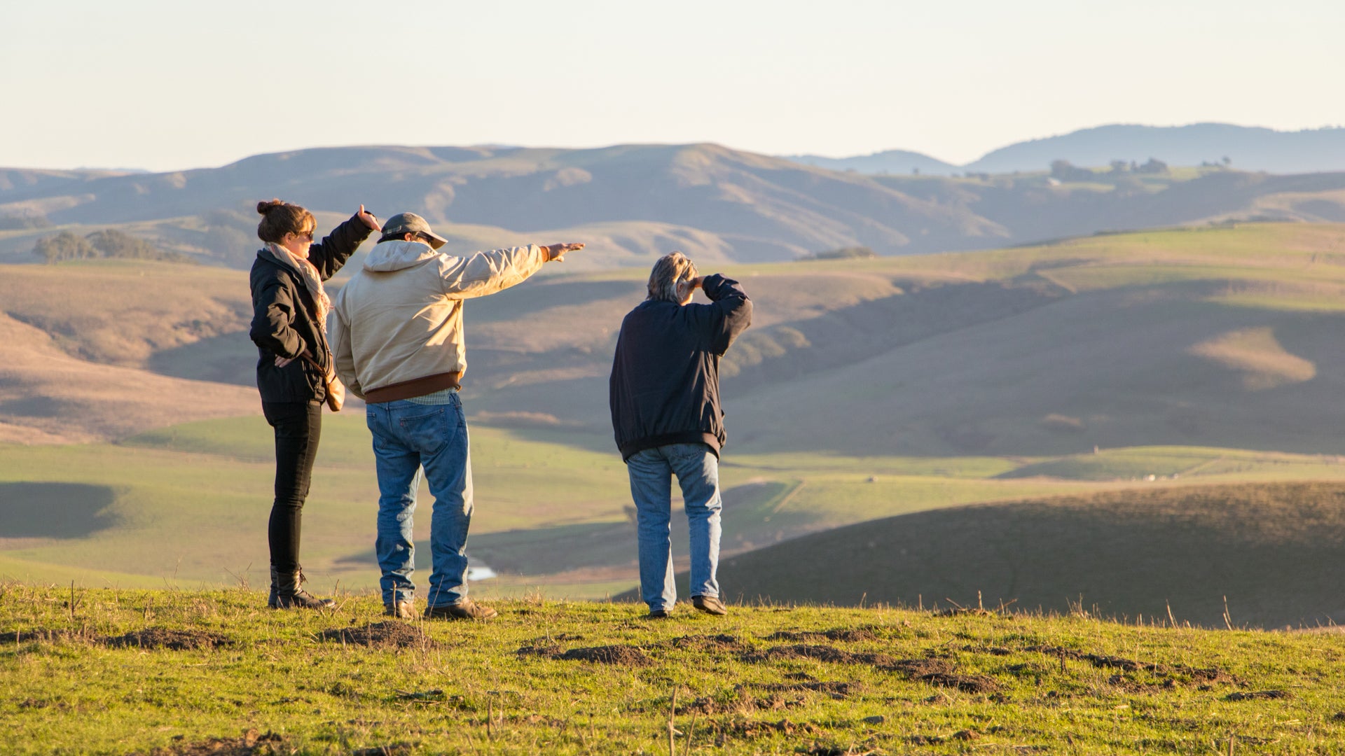 Amy, Kelsie and Joe overlooking rolling grass lands where sheep roam.