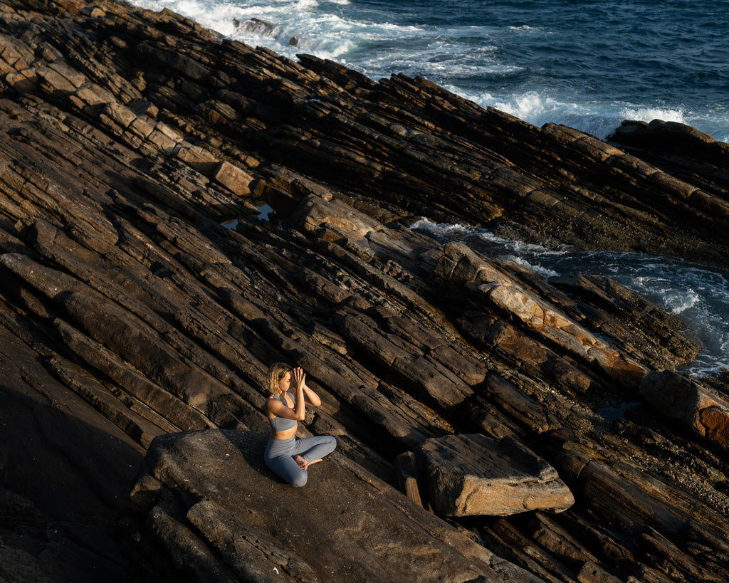 Frau meditiert auf Felsen am Meer