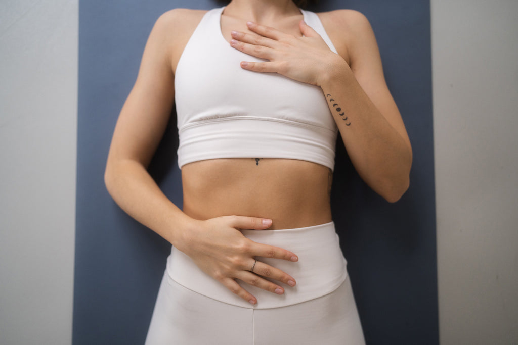Weibliche Energie im Yoga - Frau auf Yogamatte mit Händen auf Brust und Bauch