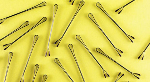 A bunch of bobby pins are scattered on a yellow background.