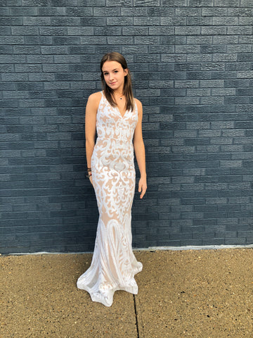 Olivia is wearing a white sheath prom gown, she is standing in front of a blue brick wall and her hair is down and straight.