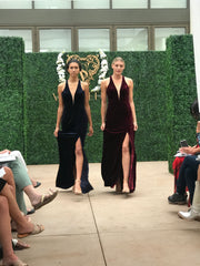 Two models walking the runway wearing dresses with a low plunge neckline and a high slit