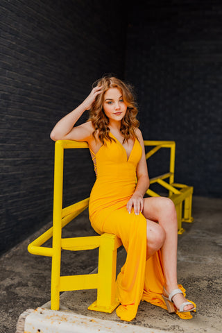 girl sitting down wearing a yellow prom dress with a slit in it