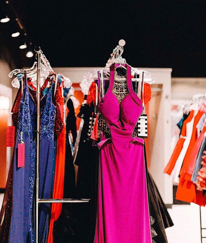 Side view of XO's dress racks. A pink sheath gown and a periwinkle sheath gown can be seen on the rack.