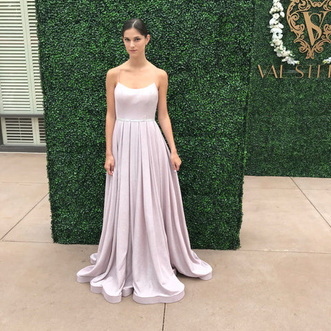 Model standing in front of an ivy wall. She is wearing a light purple A-Line gown that is simple- No sparkle, no pattern.