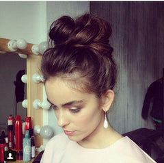 Girl with a fuller body top knot. Her head is tilted down and she is wearing pearl earrings.