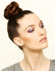 Girl with a sleek top knot bun. Her head is tilted up and she is wearing purple eye shadow.