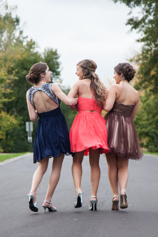 Three girls walking away in their homecoming dresses. All of their hair is done according to the back of their gown.