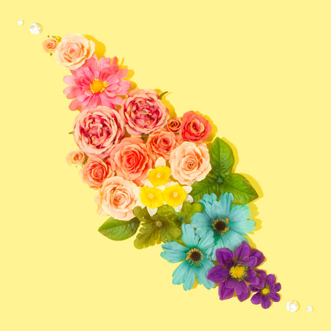 A rainbow of flowers are arranged in a diagonal diamond shape. They are on a light yellow backdrop.