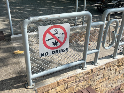 Warning sign reads "no drugs" with cannabis, cigarette and pill icons.