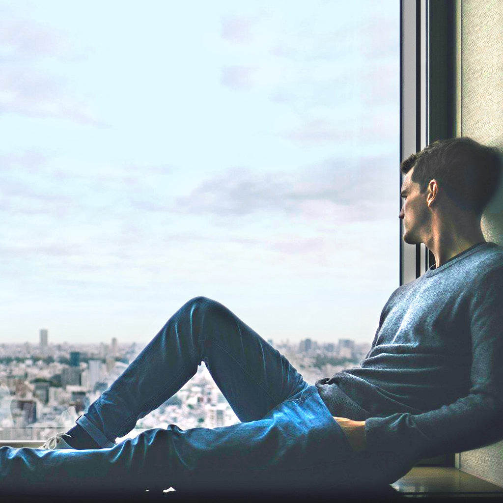 Man sitting in window sill looking out the window who is sad about his sexual performance