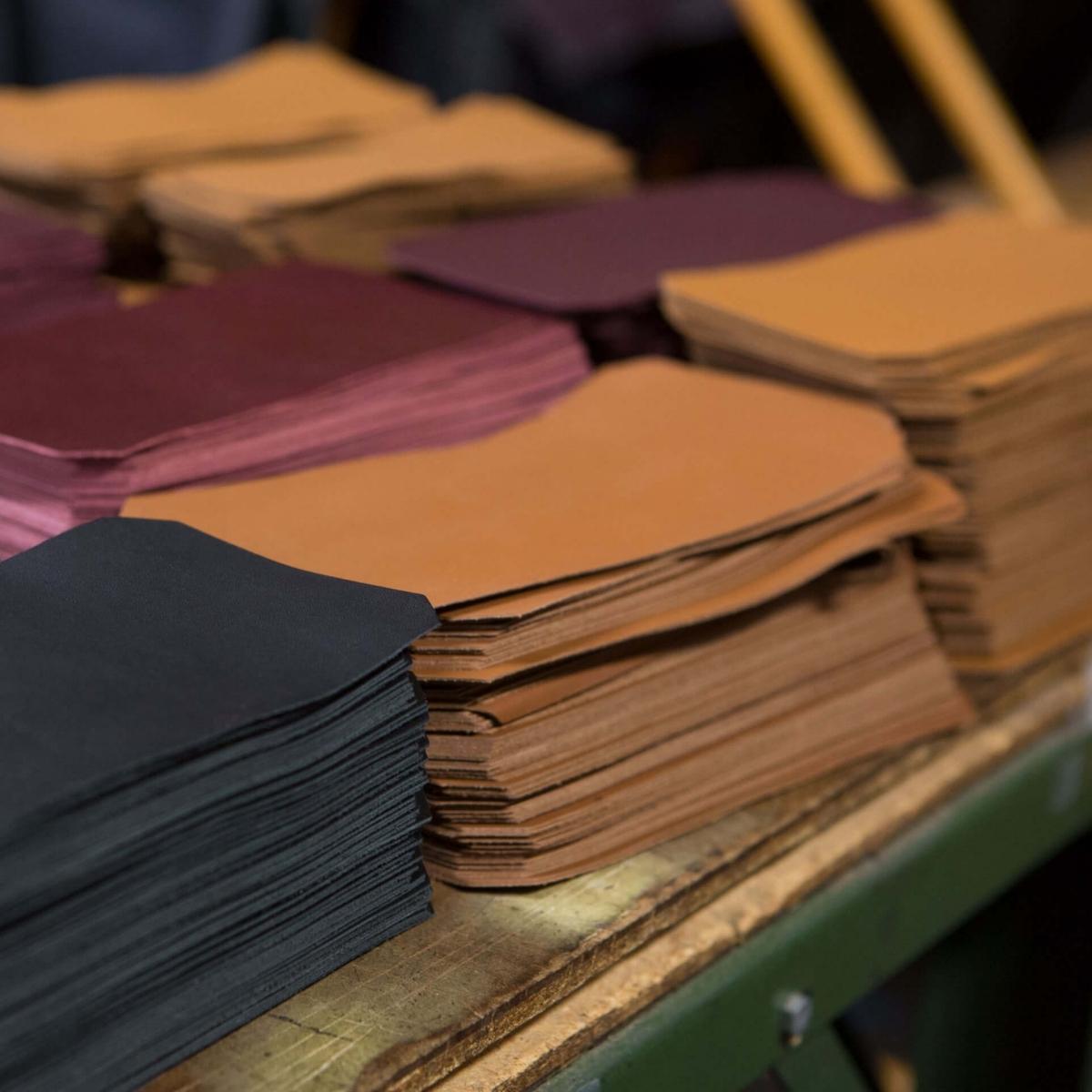 Sheets of Nappa leather used in wallet production stacked on a work table.