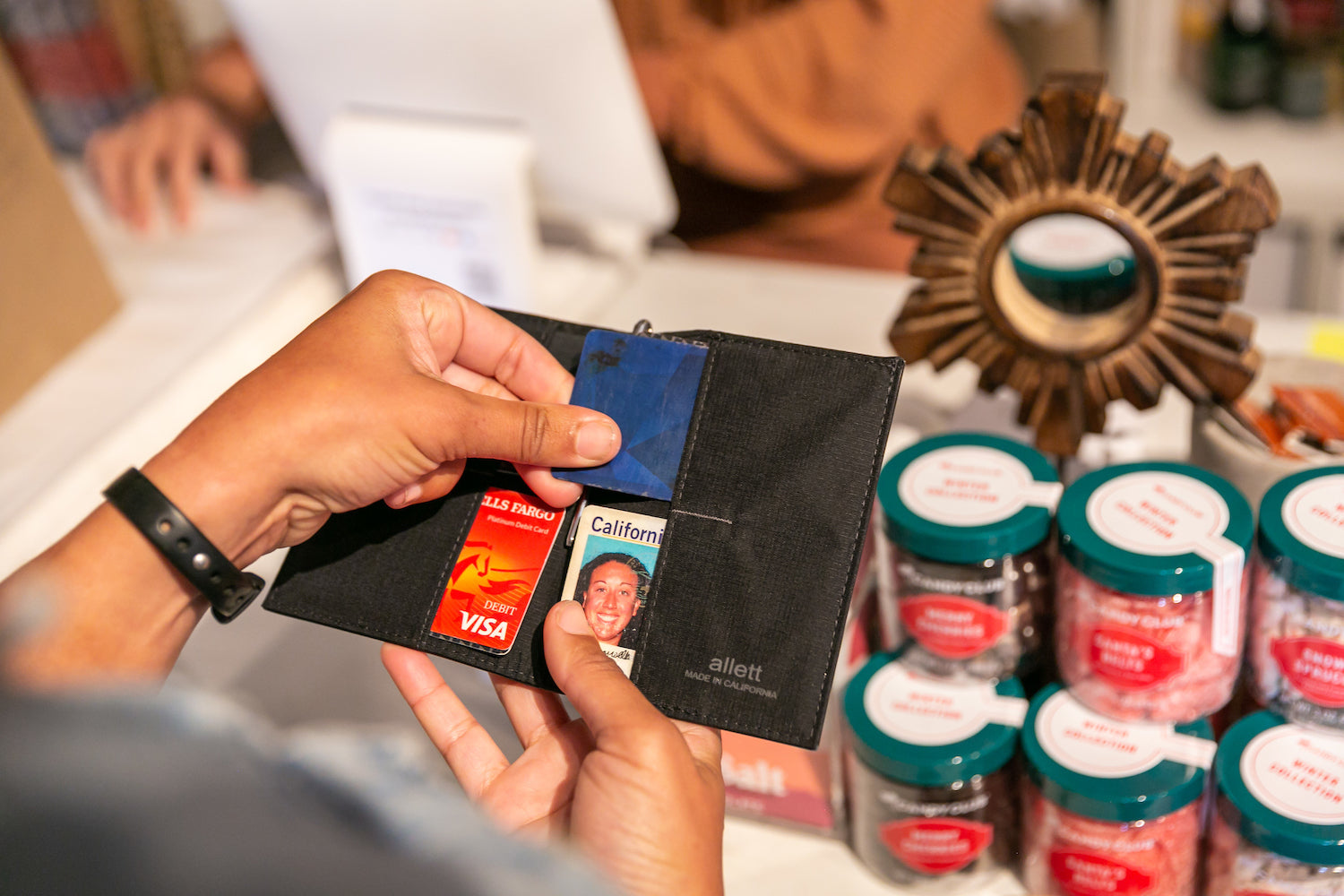 Person zieht in einem Geschäft eine Kreditkarte aus einer Allett Onyx Black Leather Original Wallet