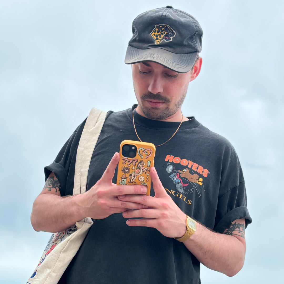 Man in cap looking at his phone with a sticker-adorned case.