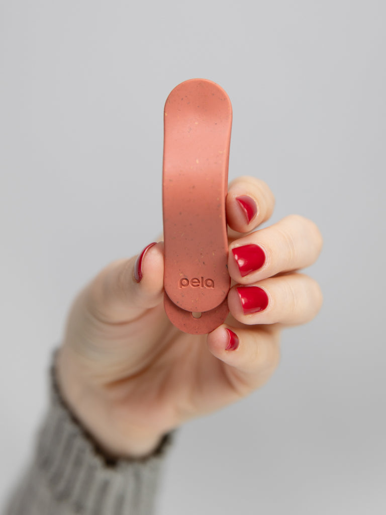 Hand holding a small, pink Pela grip with red nails.