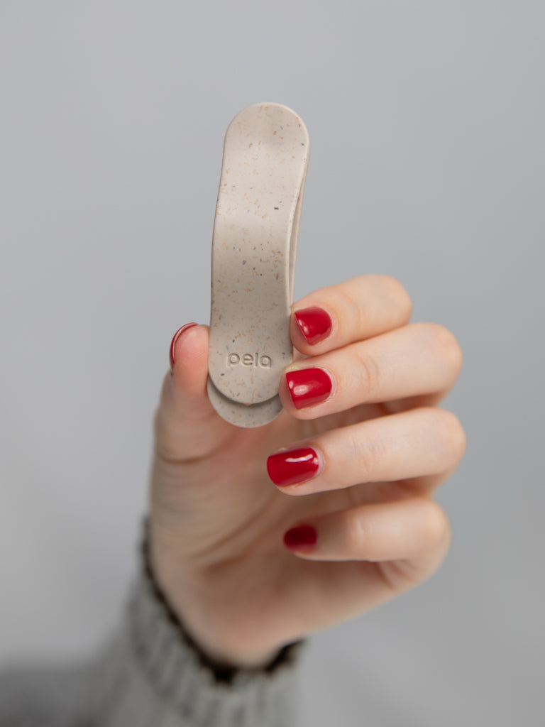Hand holding a small beige clip, nails painted red.