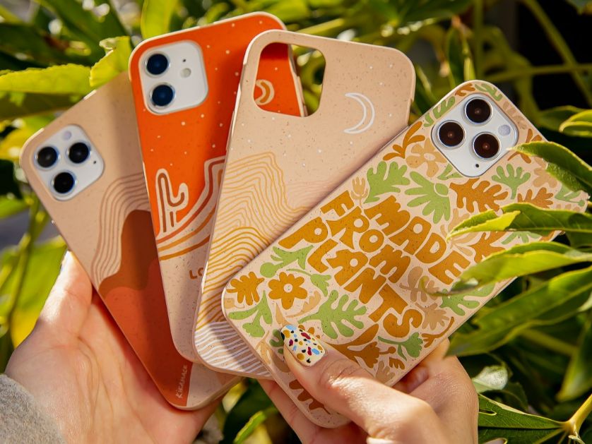 A hand holding four phone cases against an outdoor background