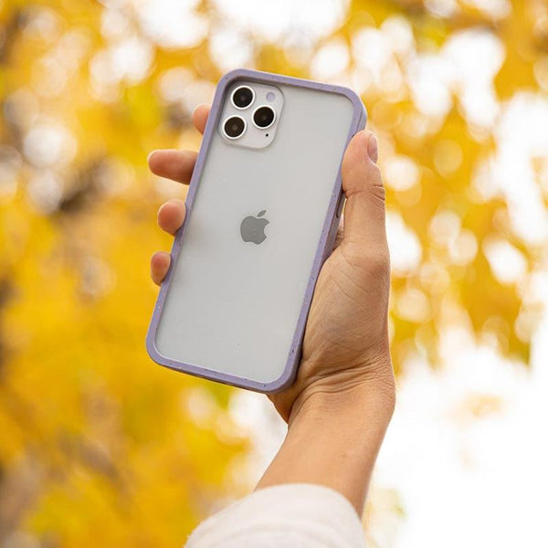 A hand holding a phone with a clear case in front of autumn trees