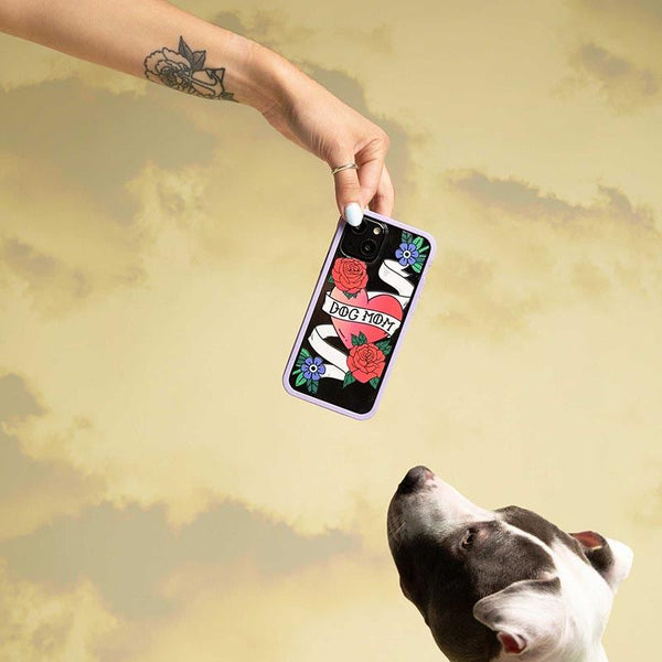 A hand holding a phone over a dog that’s looking upwards