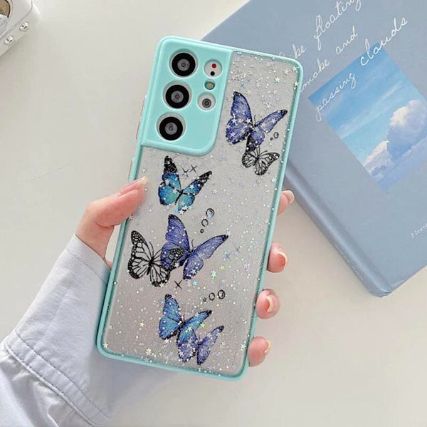 A hand holds a phone case with a blue bumper and butterflies on it