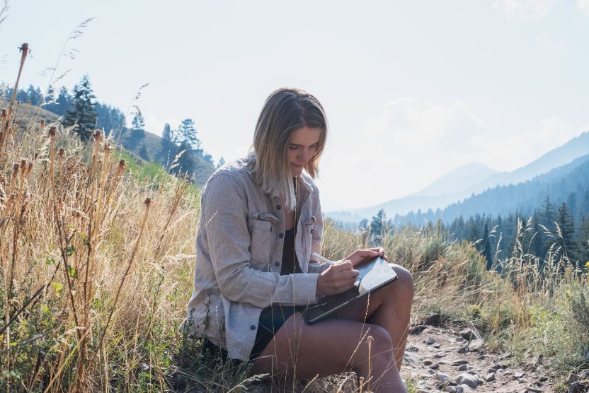 A woman working on a tablet in the woods